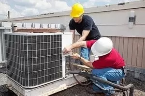 Two workers on the roof of a building working on the air conditioning unit.